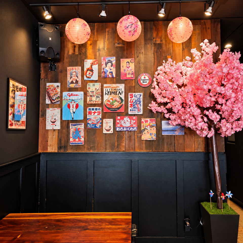 Japanese-themed restaurant interior with glowing lanterns, cherry blossom tree, vintage posters, and a wooden table.